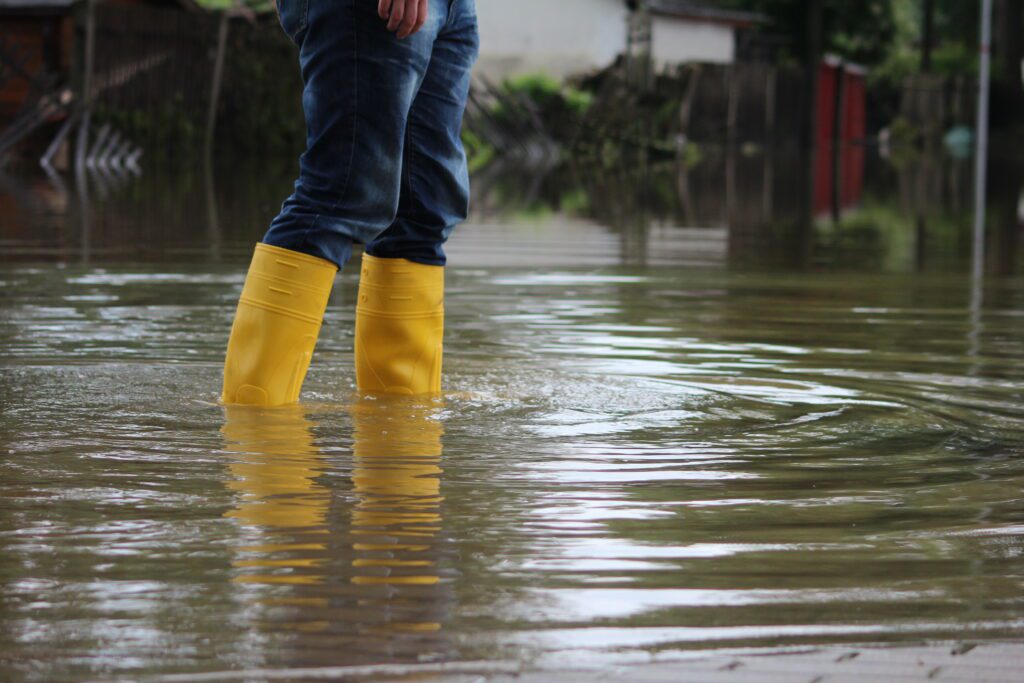 Person in yellow knee high boots standing in a flooded street where water is up to their calf