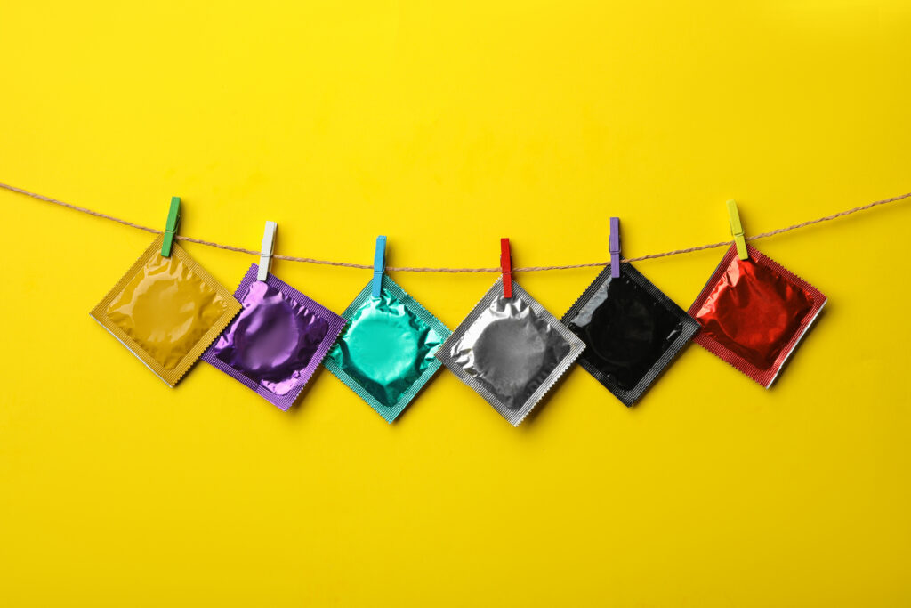 Colorful condoms hanging on clothesline against yellow background.
