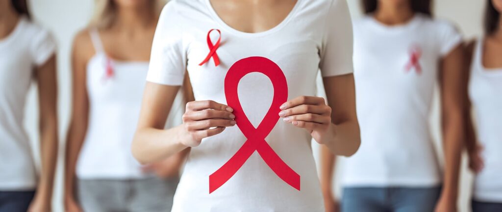 A woman in a white t-shirt holds a large red ribbon in support of STI and HIV testing and services